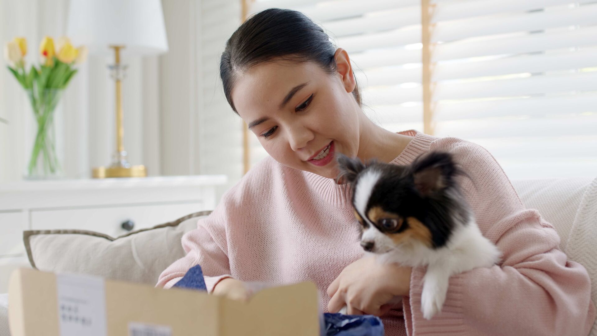 Eine Frau mit einem Chihuahua auf dem Arm öffnet ein Paket.